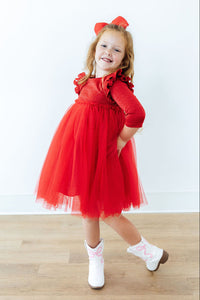 Girl wearing red shimmer 3/4 sleeve tutu dress with ruffle shoulders and white cowboy boots.
