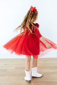 Girl twirling in a red shimmer 3/4 sleeve tutu dress with ruffled shoulders, white western boots, and a matching red hair bow.