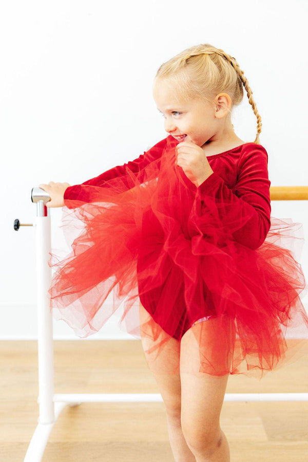 Little girl smiling at barre wearing a red velvet long sleeve leotard with a super full, fluffy多层 red tulle tutu skirt.