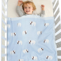 Light blue cotton baby blanket with white bears and brown scarves covering toddler in crib