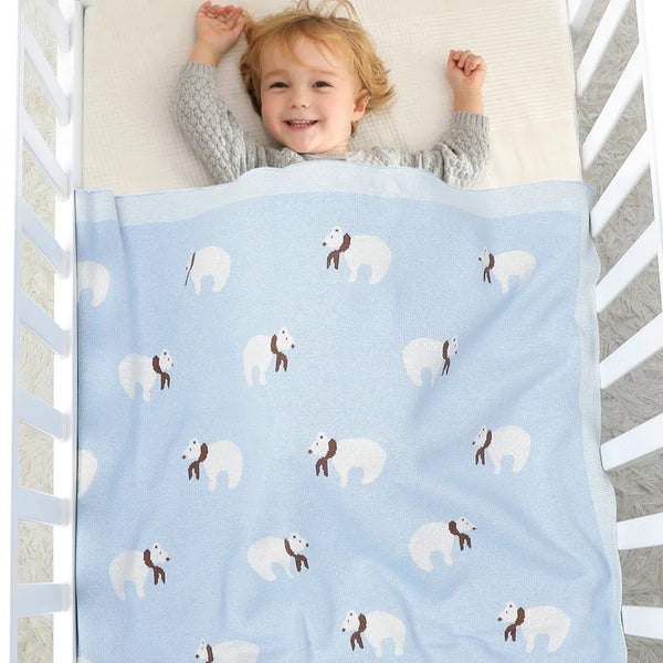 Light blue cotton baby blanket with white bears and brown scarves covering toddler in crib