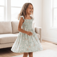 Girl wearing Mint Butterfly Daisy Bamboo Smocked Vintage Dress with flutter straps indoors.