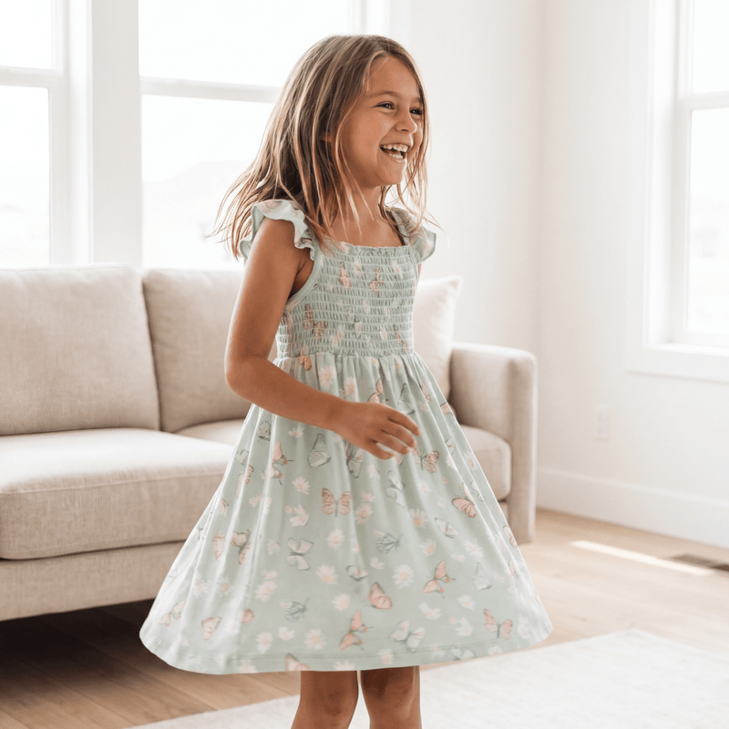 Girl wearing Mint Butterfly Daisy Bamboo Smocked Vintage Dress with flutter straps indoors.