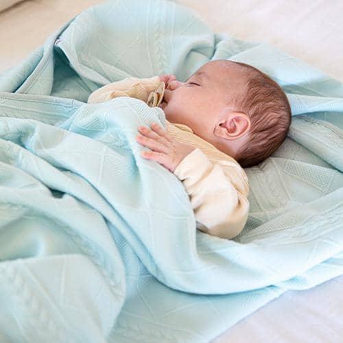 Newborn baby sleeping wrapped in a soft mint knit baby blanket on a bed