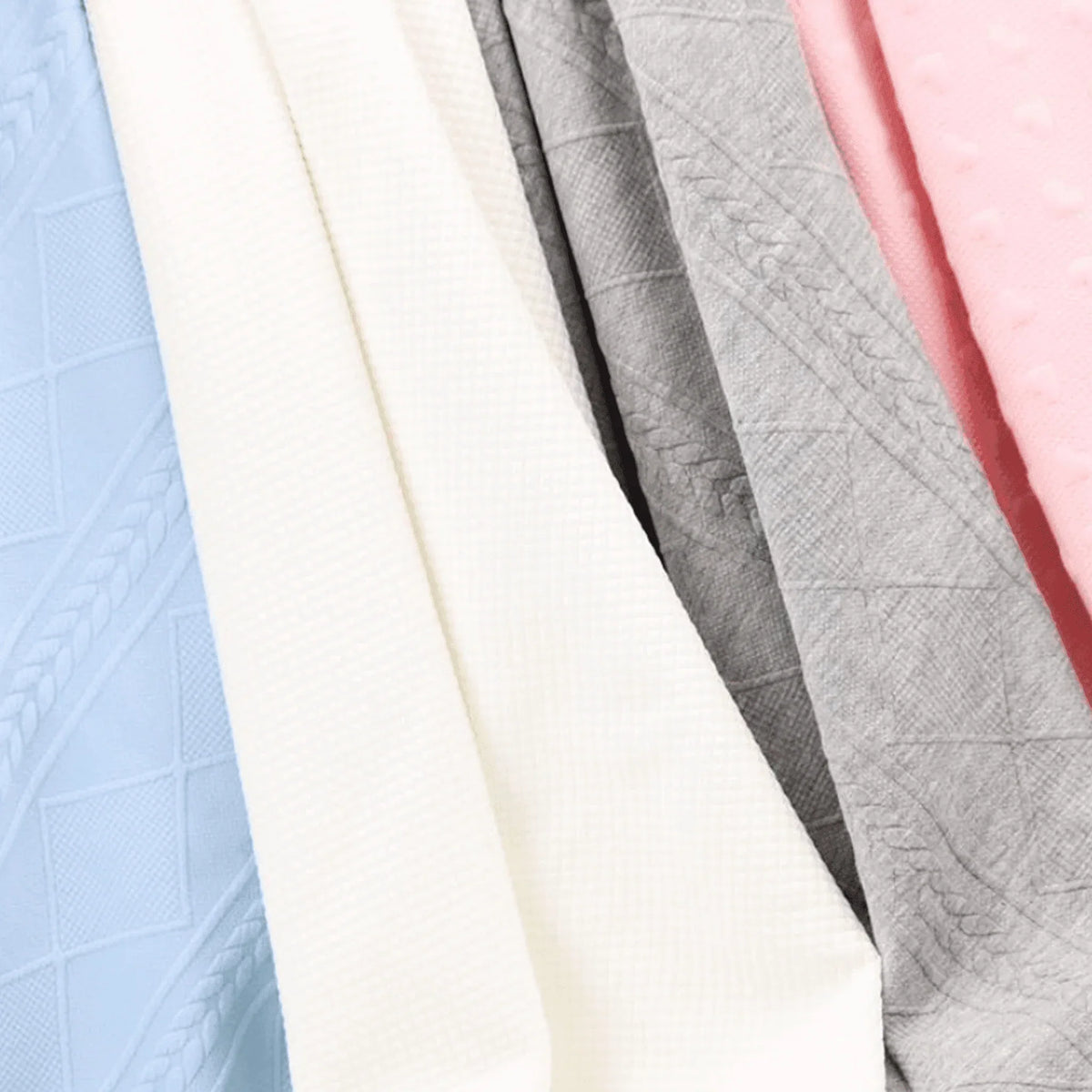Folded knit baby blankets in pastel colors including white, gray, blue, and pink for newborns