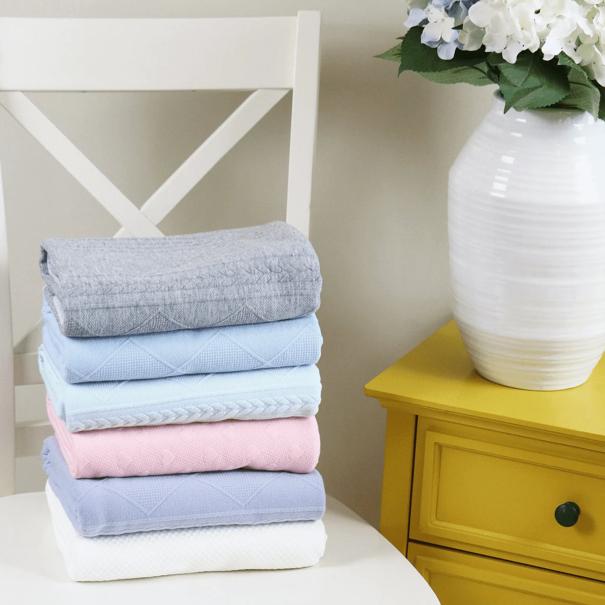 Stack of folded knit baby blankets in various colors on white chair for newborns