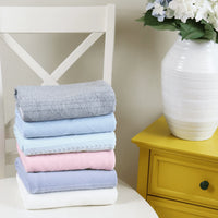 Stack of folded knit baby blankets in various colors on white chair for newborns