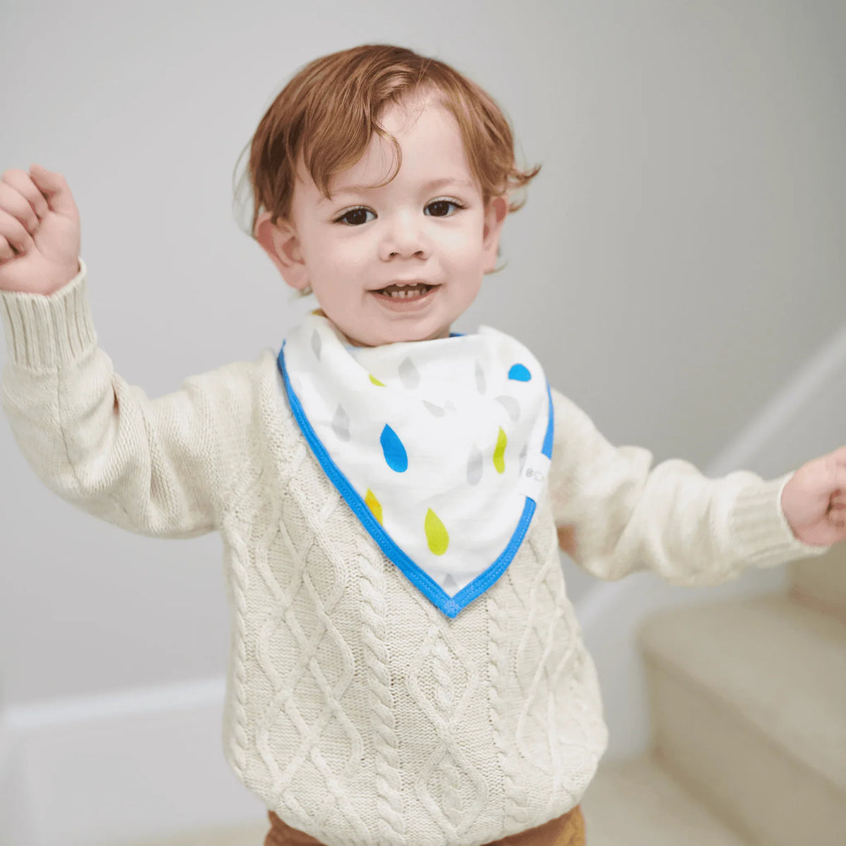 Toddler wearing white muslin and terry cloth baby bib set with blue trim and colorful raindrop pattern