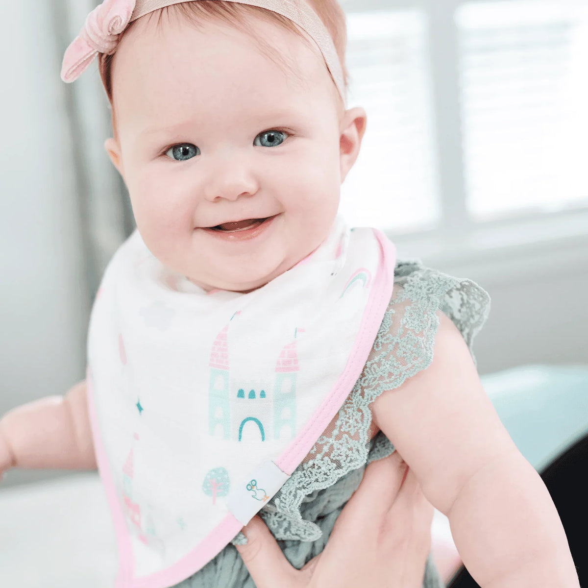 baby wearing pink and white muslin and terry cloth baby bibs with castle design smiling indoors
