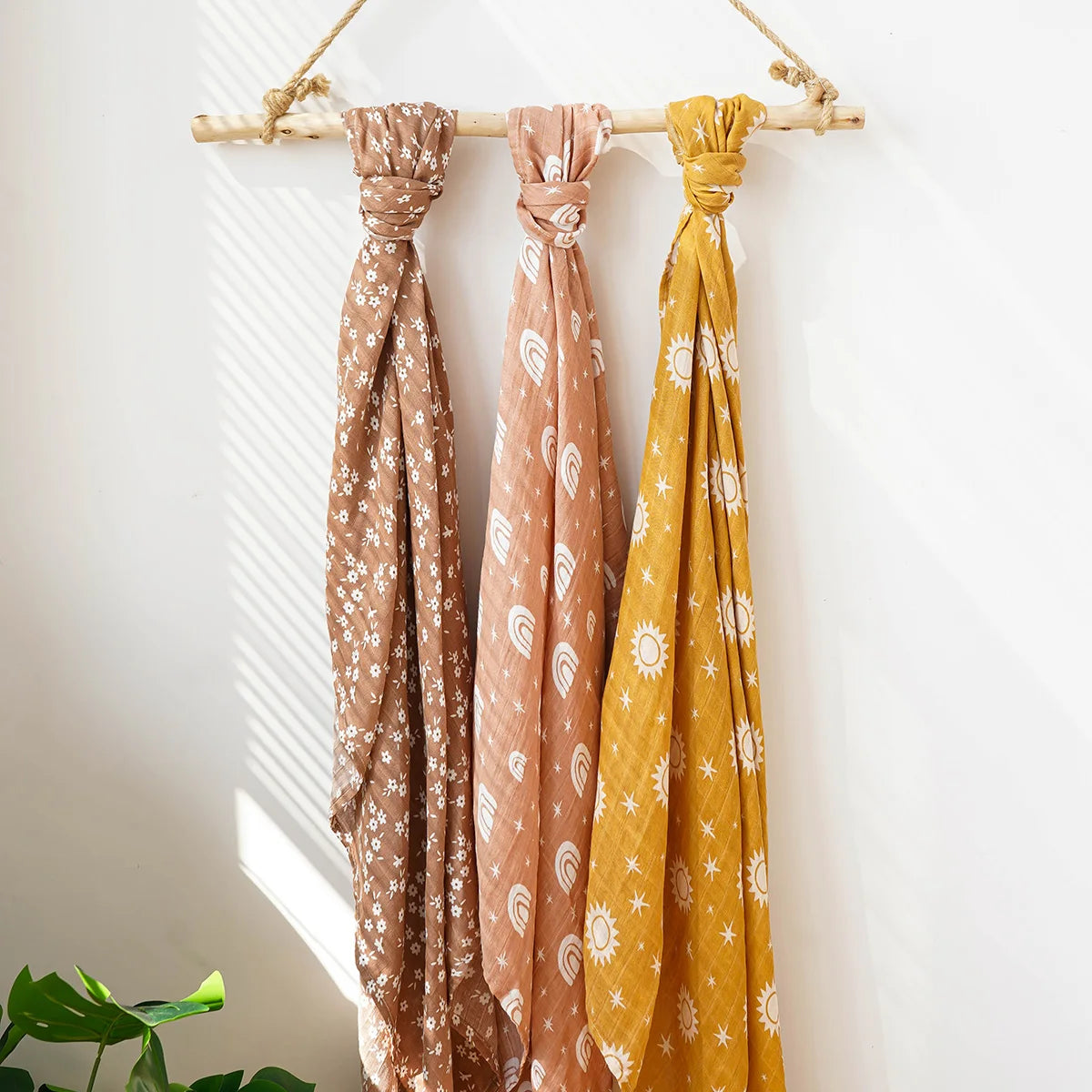 Set of three muslin swaddle blankets for babies in brown, peach, and mustard with white celestial and rainbow patterns