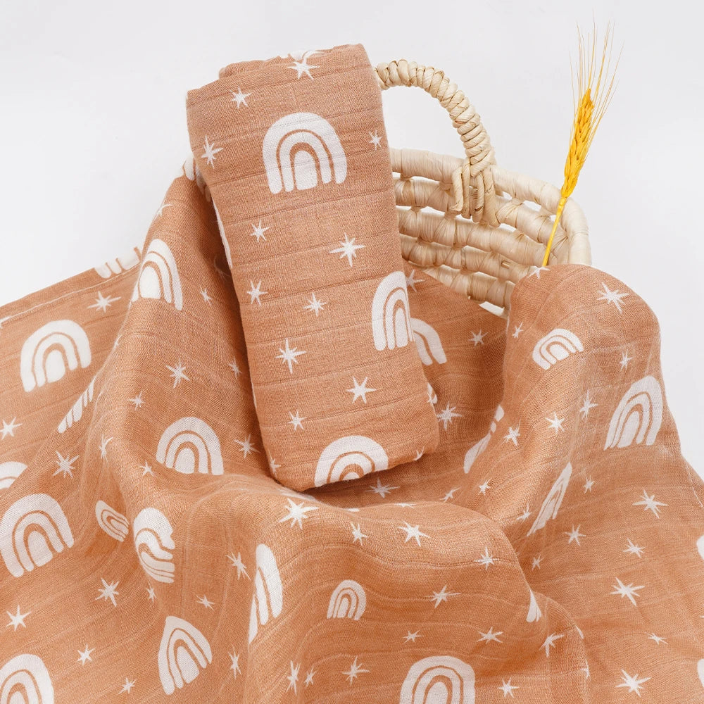 Tan muslin swaddle for babies with white rainbow and star prints, soft breathable fabric