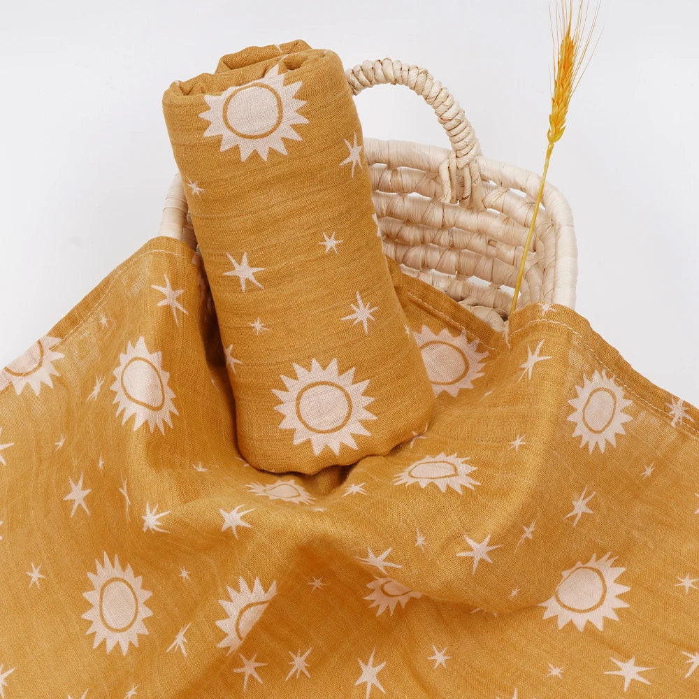 Golden yellow muslin swaddle with white sun and star print for babies in a woven basket