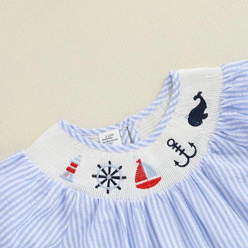 close-up of blue and white striped nautical smocked dress for girls with embroidered boat, whale, anchor, and lighthouse