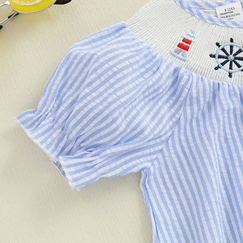 Close-up of blue and white striped nautical smocked dress for girls with embroidered lighthouse and ship wheel