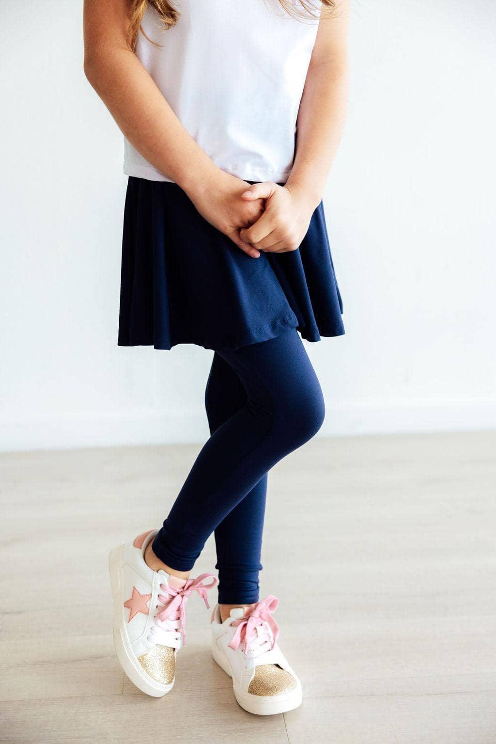 girl wearing navy twirl skegging for girls standing with legs crossed in white top and pink-laced sneakers