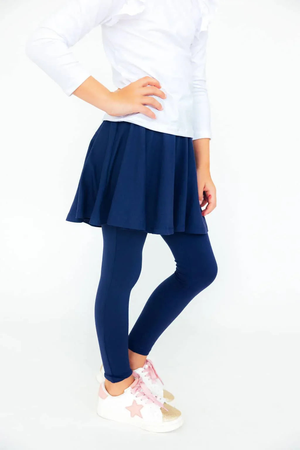 Girl wearing navy twirl skegging for girls standing with hand on hip in white top and pink star sneakers