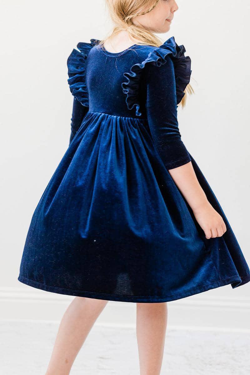 young girl wearing navy velvet ruffle dress for girls twirling in studio
