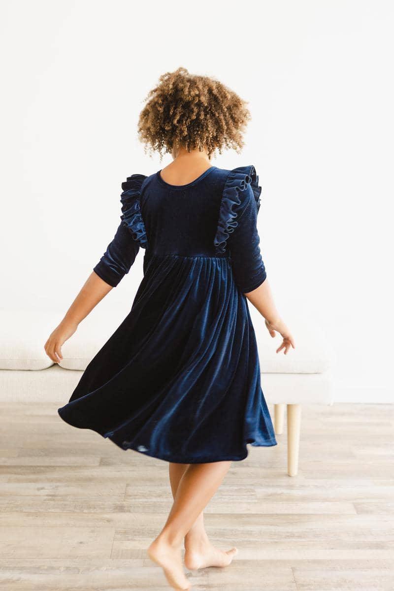 girl wearing navy velvet ruffle dress for girls twirling barefoot on wooden floor