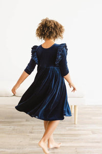 girl wearing navy velvet ruffle dress for girls twirling barefoot on wooden floor