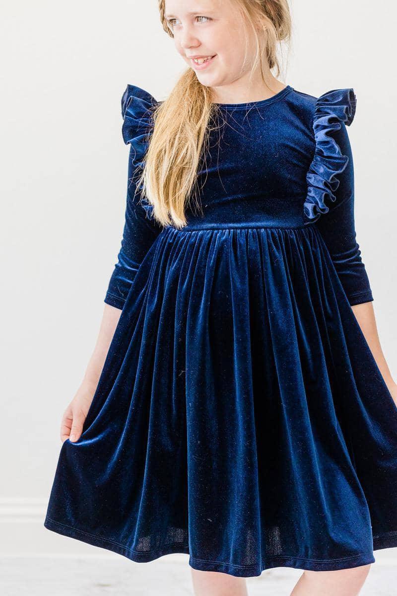 girl wearing navy velvet ruffle dress for girls standing and holding dress hem