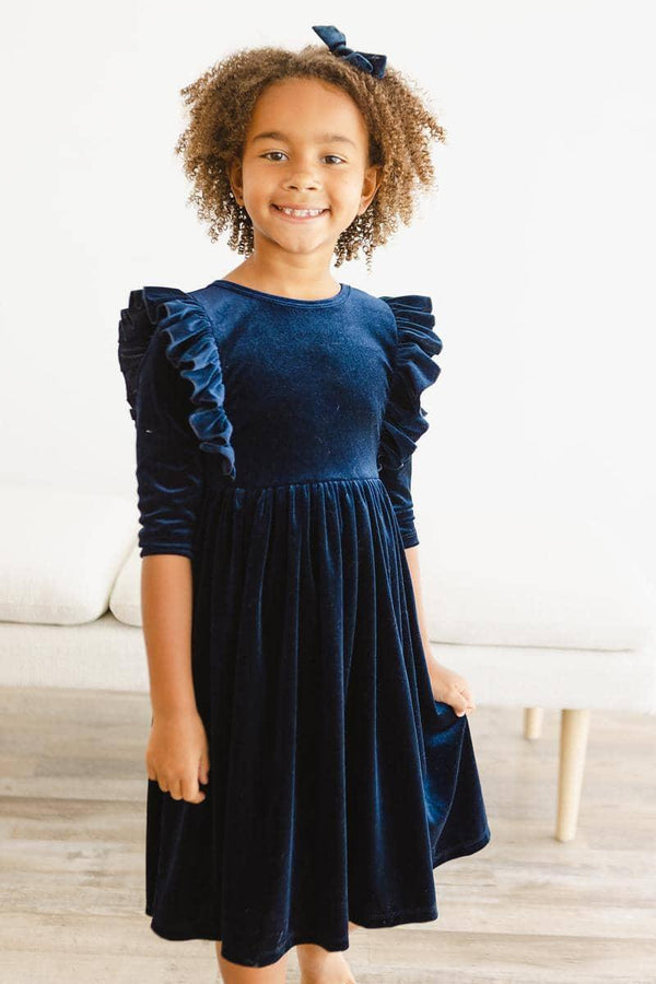 girl wearing navy velvet ruffle dress for girls standing and smiling indoors