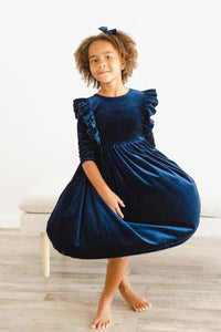 girl wearing navy velvet ruffle dress for girls twirling indoors barefoot with matching hair bow