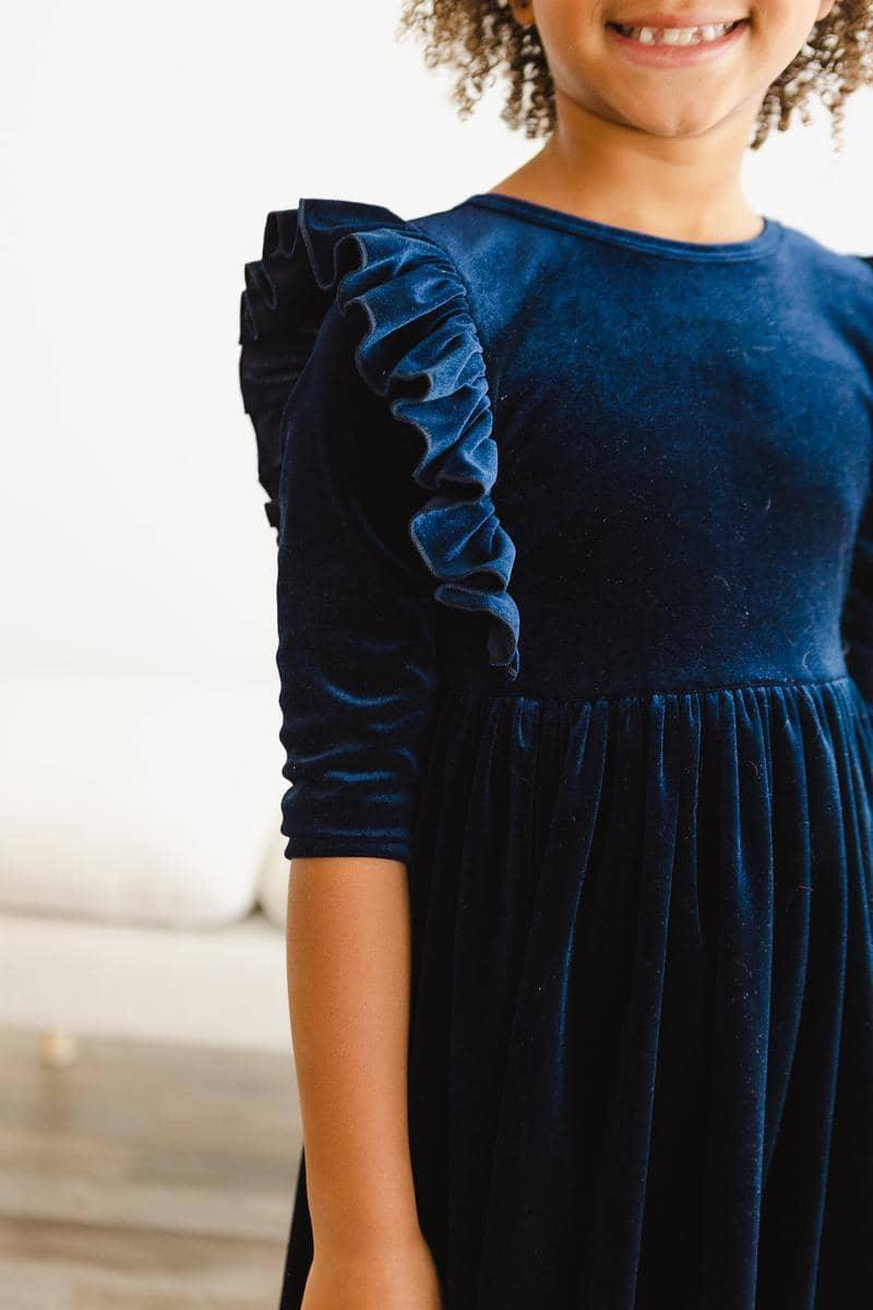 young girl wearing navy velvet ruffle dress for girls with long sleeves standing indoors