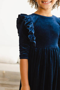 young girl wearing navy velvet ruffle dress for girls with long sleeves standing indoors