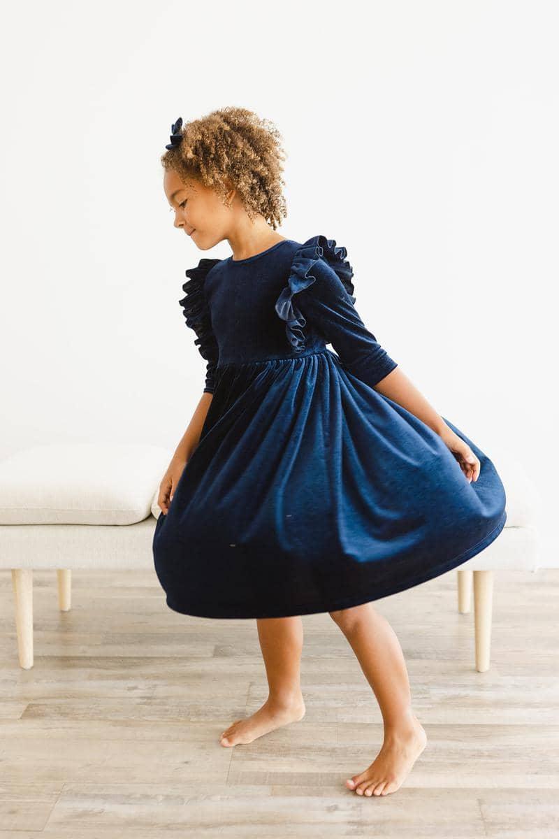 Young girl wearing navy velvet ruffle dress for girls twirling barefoot indoors