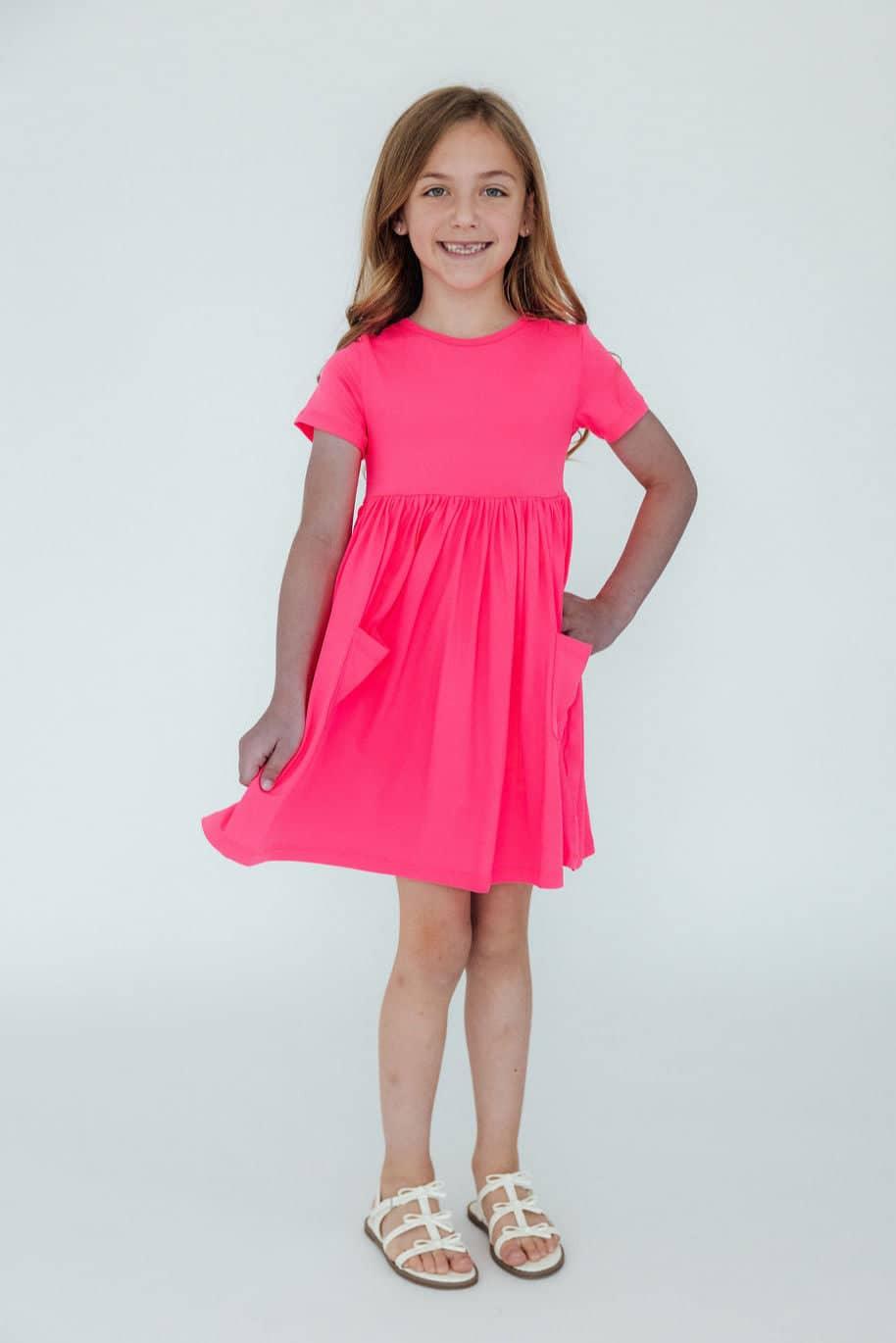 Girl wearing neon pink girls twirl dress standing and smiling with hands on pockets