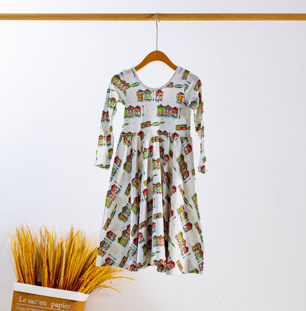 Kid's dress with a colorful houses print hanging on a wooden hanger.