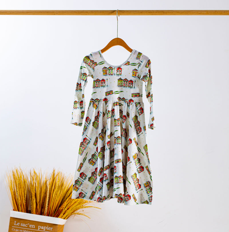 Kid's dress with a colorful houses print hanging on a wooden hanger.
