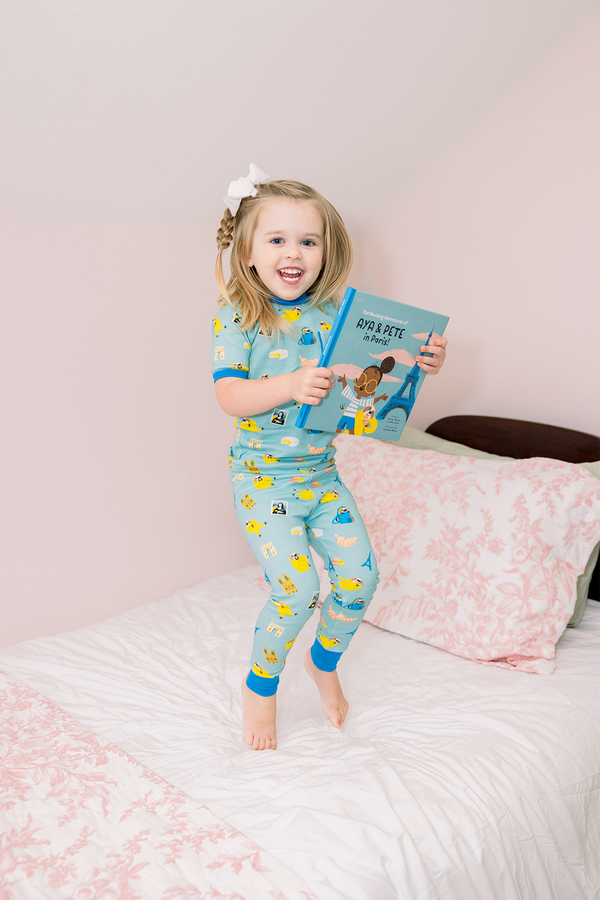 Little girl in turquoise Aya & Pete in Paris organic cotton pajamas holding the Paris-themed book from the set.