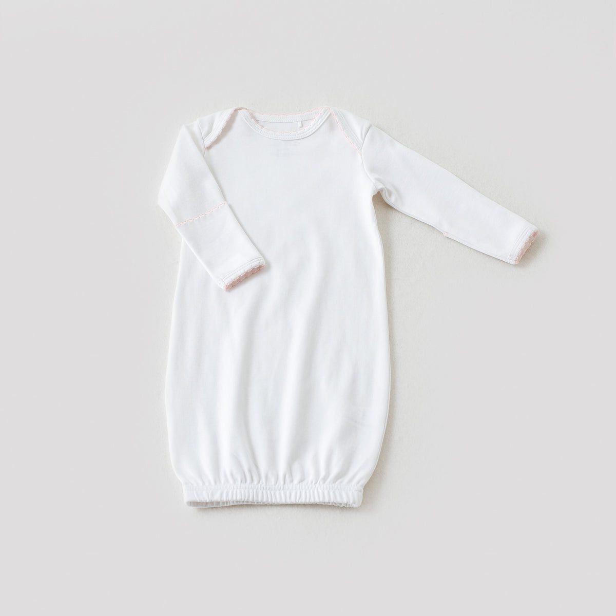 White newborn take me home gown with baby pink trim, featuring long sleeves and an elastic hem for elegant, easy diaper access.