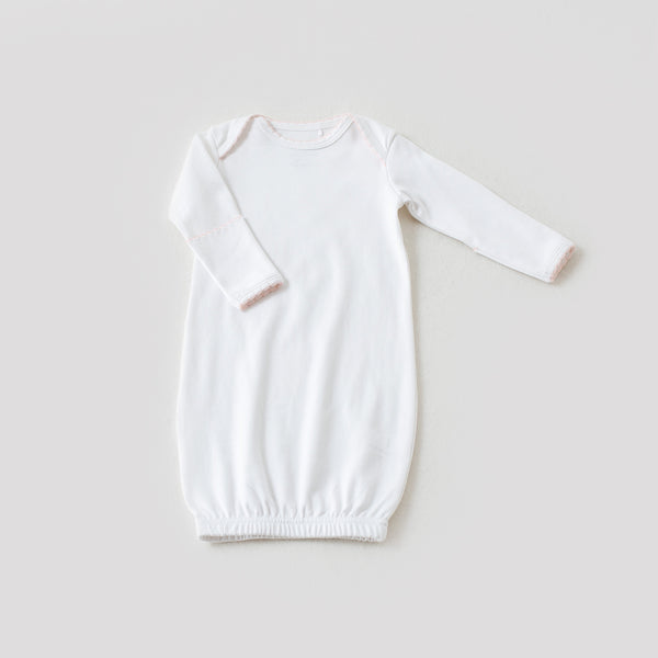 White newborn take me home gown with baby pink trim, featuring long sleeves and an elastic hem for elegant, easy diaper access.
