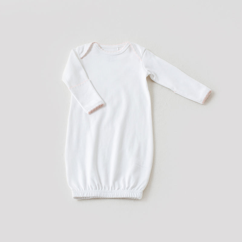 White newborn take me home gown with baby pink trim, featuring long sleeves and an elastic hem for elegant, easy diaper access.
