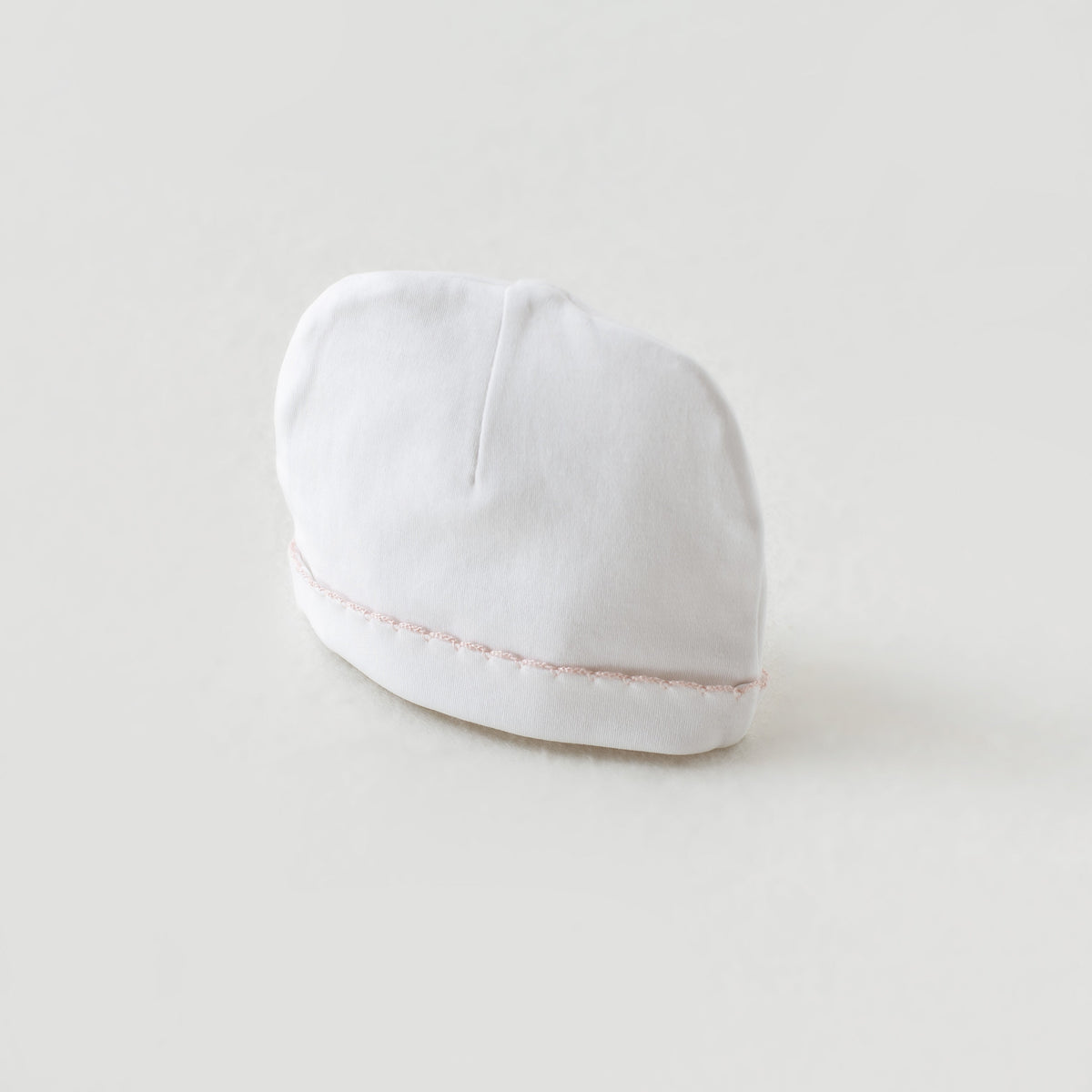 White newborn beanie hat with delicate baby pink stitched trim, part of the Take Me Home Set.