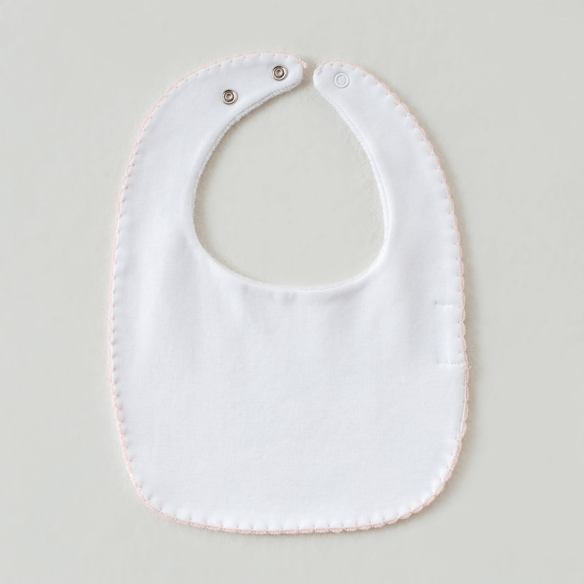 White baby bib with pink hem and snap closures from the Pink Newborn Take Me Home Set.