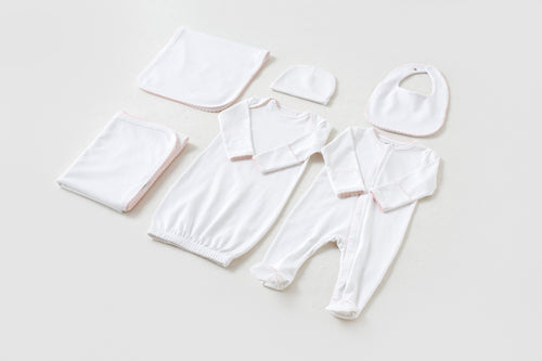 White newborn take me home set with pink trim, including gown, footed pajama, hat, bib, and blankets.