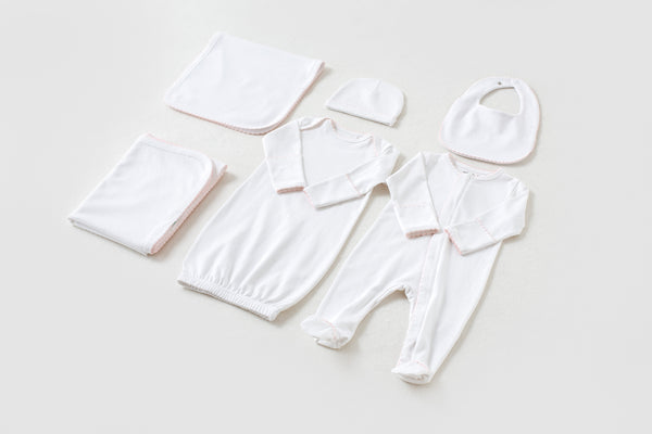 White newborn take me home set with pink trim, including gown, footed pajama, hat, bib, and blankets.