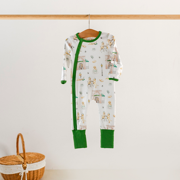 Baby onesie with green trim hanging on a wooden hanger against a white wall.