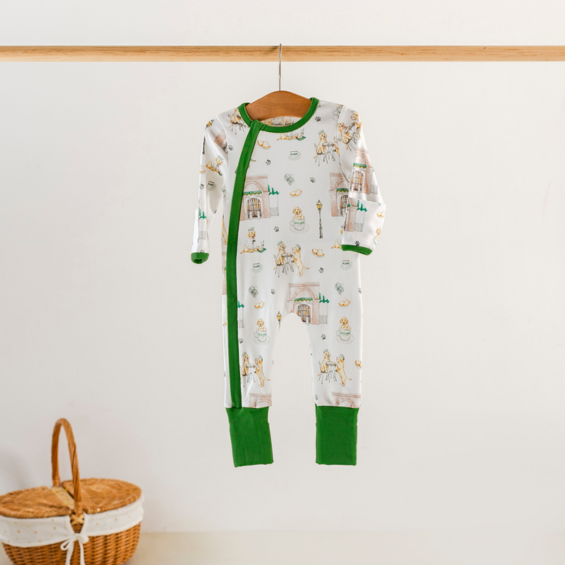 Baby onesie with green trim hanging on a wooden hanger against a white wall.