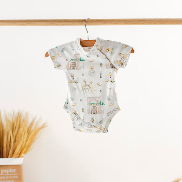 Baby onesie with cityscape pattern hanging on a wooden hanger against a white background.