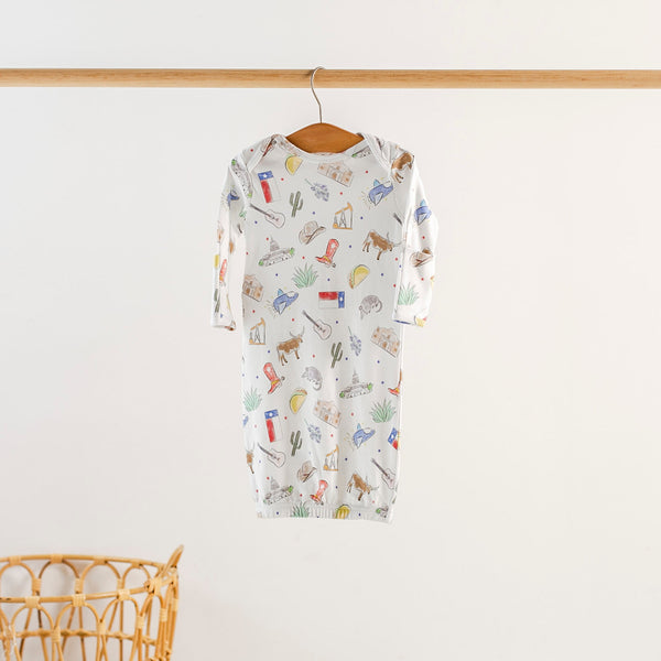 Texas Kids Organic Cotton sleepwear in three styles (newborn gown, zipper romper, two-piece set) on a wooden hanger.