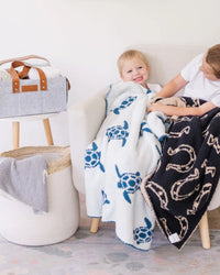 Smiling toddler wrapped in reversible sea turtle baby blanket featuring blue turtles on white and patterned navy side.