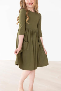 Girl wearing olive twirl dress for girls with 3/4 sleeves and pockets spinning indoors