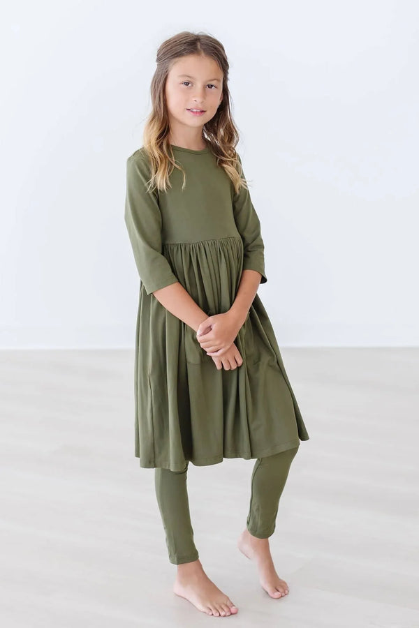 Girl wearing olive twirl dress for girls with three quarter sleeves standing barefoot indoors