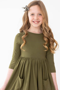 young girl wearing olive twirl dress for girls with 3/4 sleeves and pockets smiling