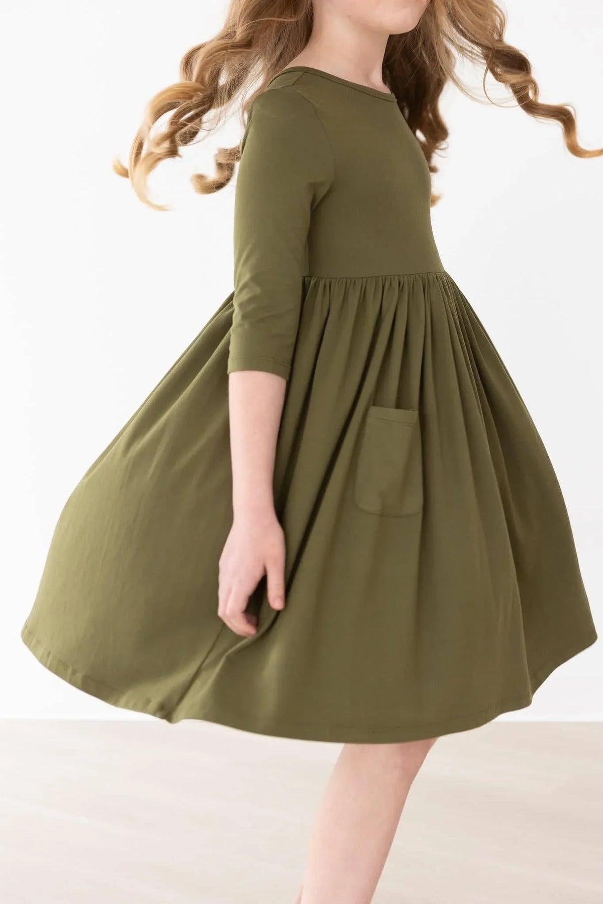 Young girl wearing olive twirl dress for girls by Mila Rose spinning to show pockets