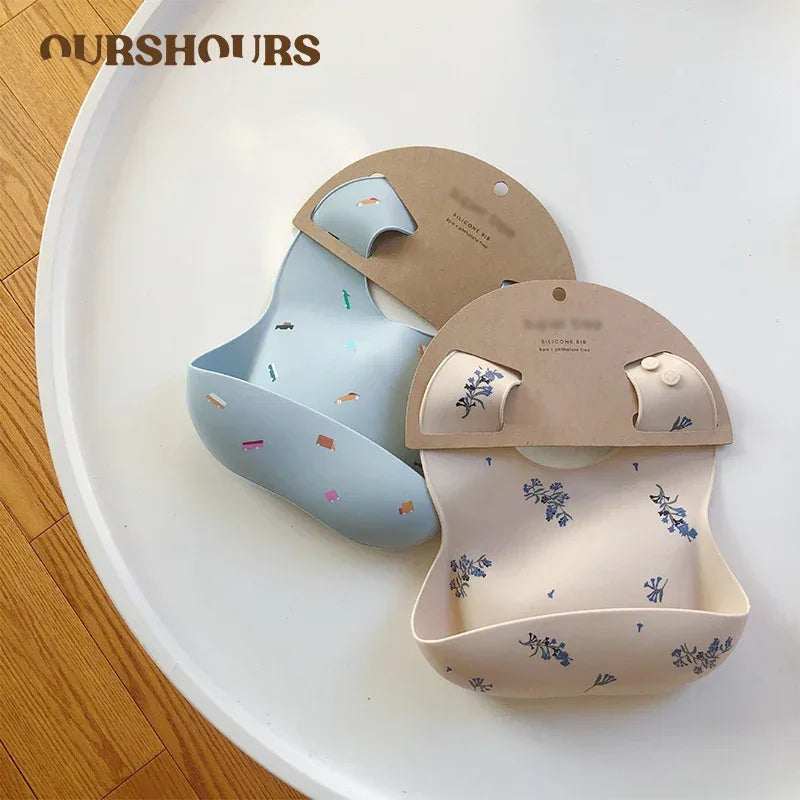 Two waterproof baby bibs in blue and cream with floral print designed for babies and toddlers